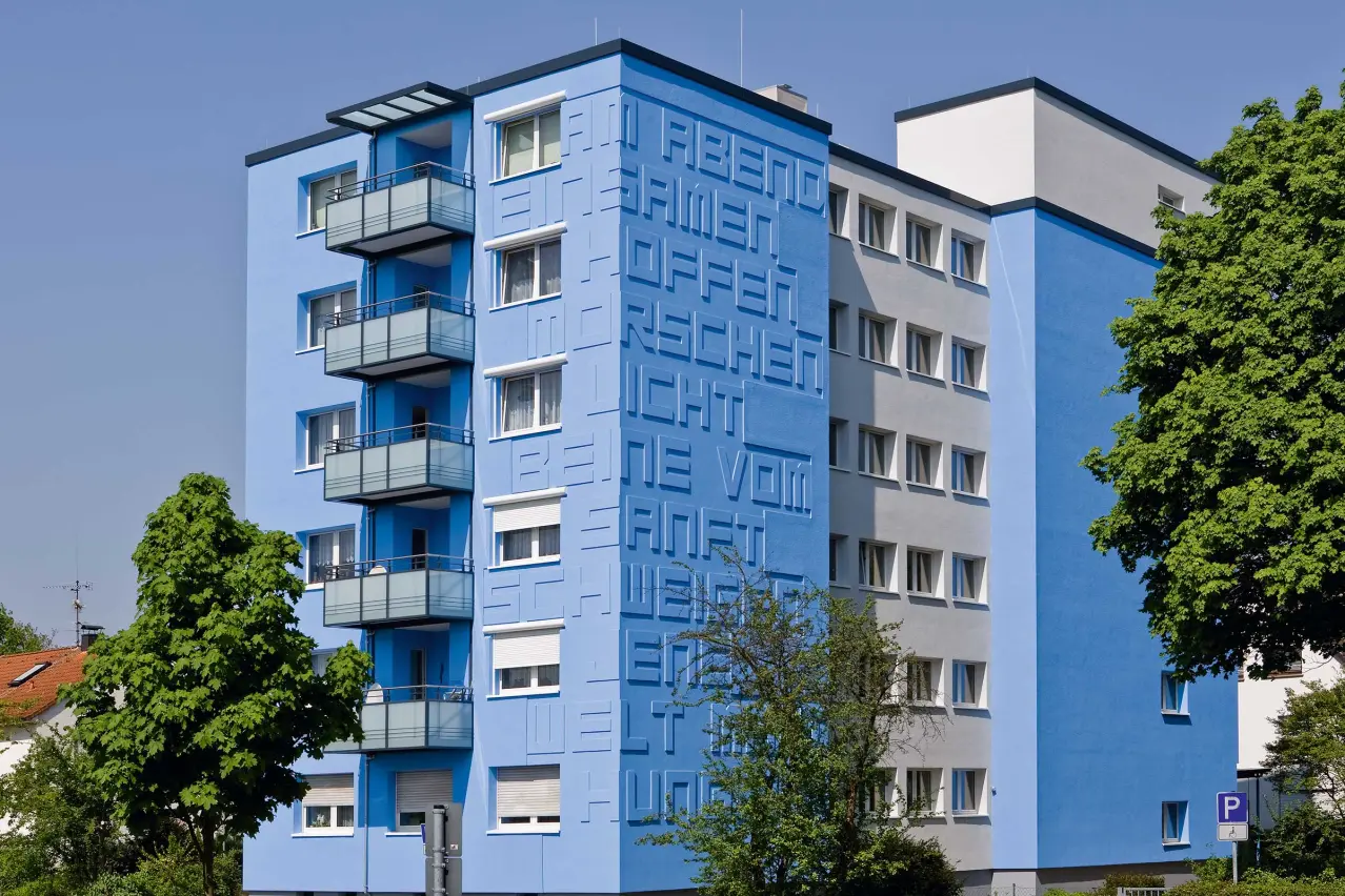 Bloc de locuințe cu fațadă albastră, cu litere StoDeco decupate din plăci Decoplan